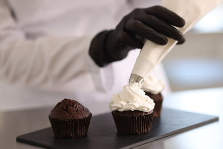 Confectioner decorating cupcake with cream at table, closeupの写真素材