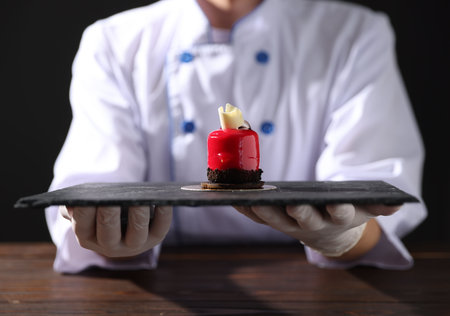 Confectioner with tasty dessert at wooden table against black background, closeupの写真素材