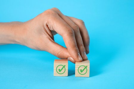 Woman touching cube with check mark on light blue, closeupの写真素材