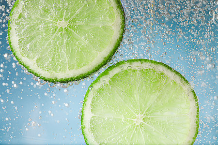 Soda water with lime slices against light blue background, closeup
