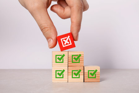 Rejected. Woman choosing cube with cross among other ones with check marks at table, closeup