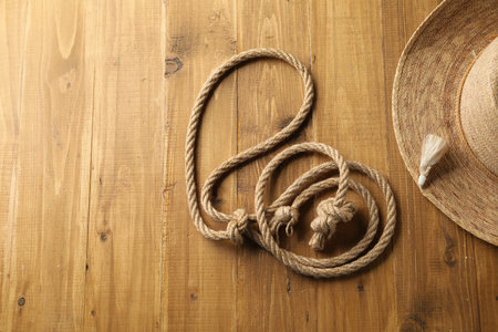 Lasso made of cotton rope and straw hat on wooden background, flat lay. Space for textの写真素材