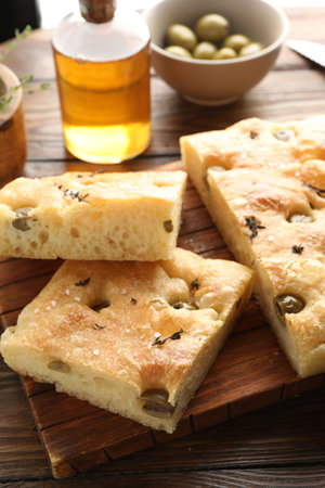 Pieces of delicious focaccia bread with olives, thyme, oil and salt on wooden table, closeupの写真素材