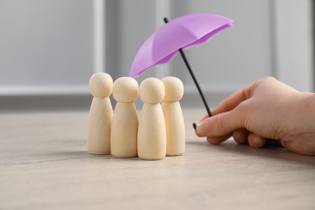 Woman holding umbrella over human figures at light wooden table, closeup. Insurance conceptの写真素材