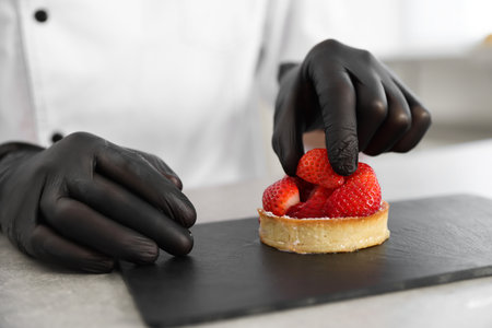 Confectioner decorating tart with strawberry at grey table in kitchen, closeupの写真素材