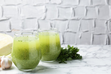 Healthy parsley smoothie in glasses, garlic and leaves on white marble table against grey textured background, closeup. Space for textの写真素材