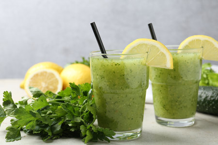 Healthy parsley smoothie in glasses, leaves and lemon on light textured table against grey background, closeupの写真素材