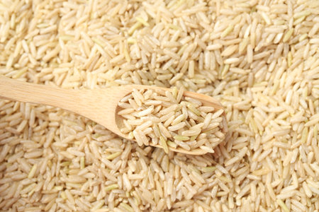 Brown rice in wooden spoon over pile of grains, top viewの写真素材