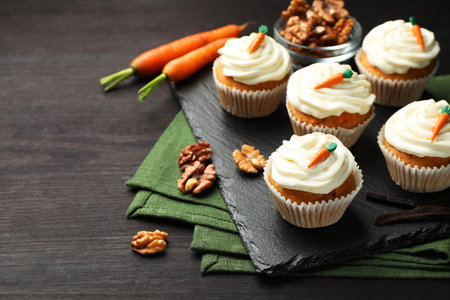 Tasty carrot muffins with cream, walnuts and fresh vegetables on black wooden table, closeup. Space for textの写真素材