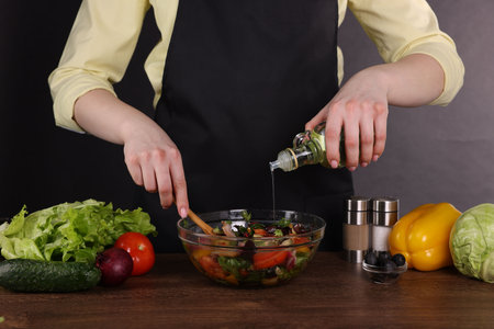Woman pouring oil onto tasty salad at wooden table against dark background, closeupの写真素材