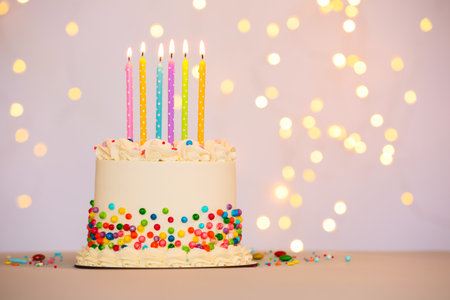 Tasty cake with colorful sprinkles and candles on table against light background, space for text. Bokeh effectの写真素材