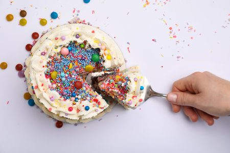 Woman taking piece of tasty bento cake with colorful sprinkles on white background, top viewの写真素材