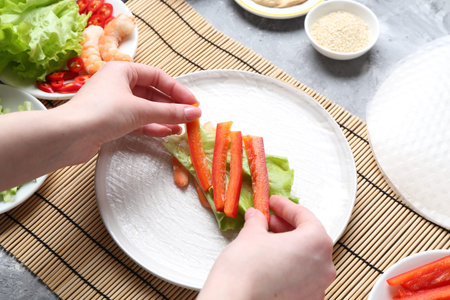Woman making tasty spring roll at light grey table, above view