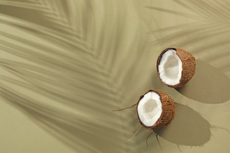 Fresh coconut and shadow cast by tropical palm on light green background, top view. Space for textの写真素材