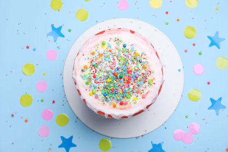 Delicious cake, confetti and sprinkles on light blue table, flat lay