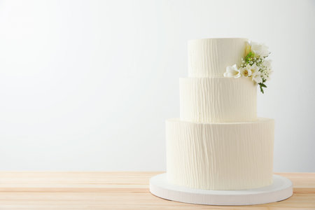 Delicious wedding cake with floral decor on wooden table against white background, space for textの写真素材
