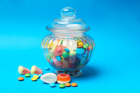 Different tasty candies in glass jar on light blue background, closeupの写真素材