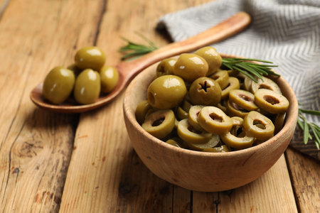 Delicious marinated olive rings in bowl, spoon and rosemary on wooden table, closeupの写真素材