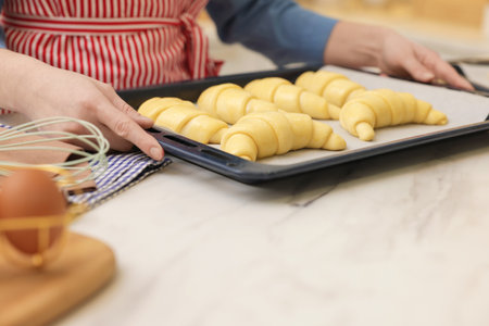 Woman taking baking sheet with raw croissants out of white marble table, closeupの写真素材