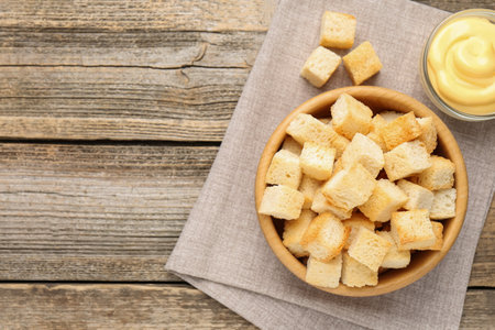 Tasty crispy croutons in bowl and sauce on wooden table, top view. Space for textの写真素材