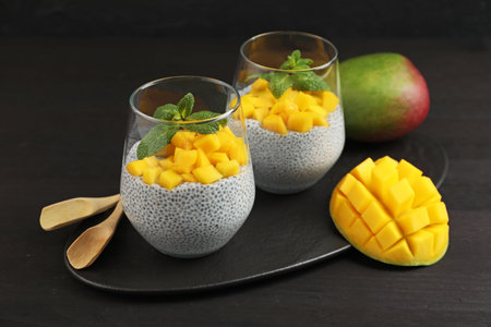 Delicious chia pudding with mango and mint in glasses on dark wooden tableの写真素材
