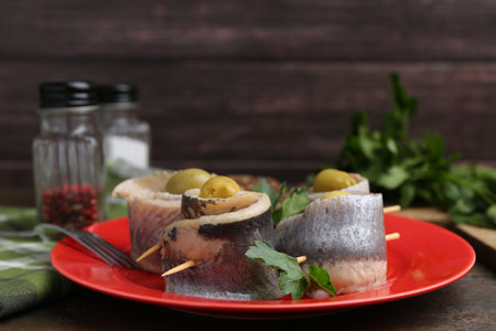 Delicious herring rolls with olives and parsley on wooden table, closeupの写真素材