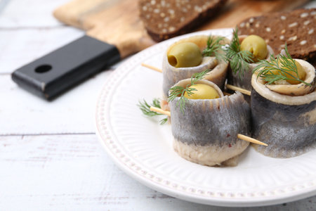 Delicious herring rolls with olives, dill and bread on white wooden table, closeup. Space for textの写真素材