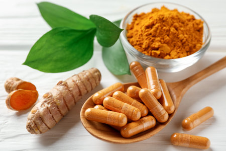 Turmeric capsules, powder, roots and green leaves on white wooden table, closeupの写真素材