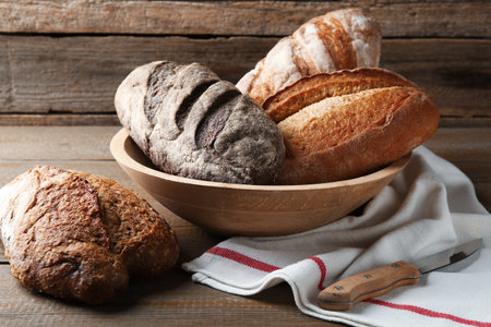Different loaves of fresh bread and knife on wooden table