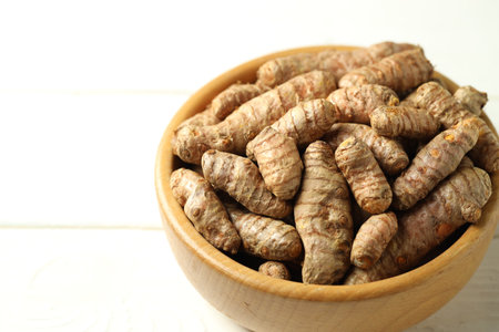 Tumeric rhizomes in bowl on white wooden table, closeupの写真素材