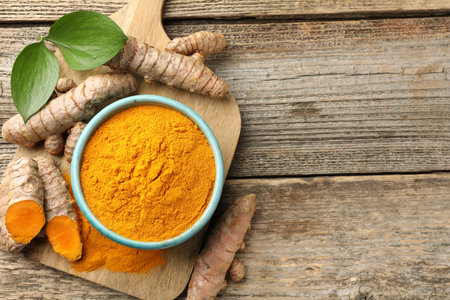 Turmeric powder in bowl, roots and leaves on wooden table, flat lay. Space for textの写真素材