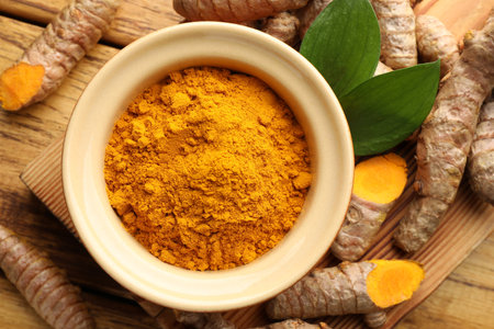 Turmeric powder in bowl, roots and leaves on wooden table, flat layの写真素材