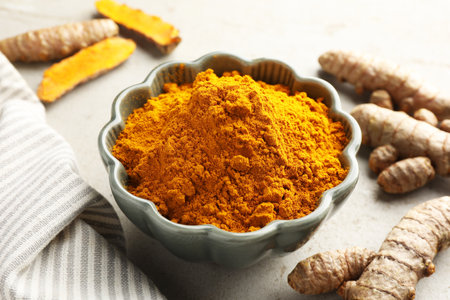 Aromatic turmeric powder in bowl and fresh roots on light grey table, closeupの写真素材