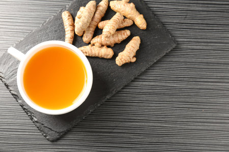 Aromatic turmeric tea and rhizomes on black table, top view. Space for text
