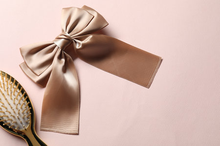 Beautiful hair bow and brush on pale pink background, flat lay. Space for textの写真素材