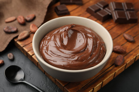 Tasty pudding in bowl, pieces of chocolate and cocoa beans on black table, closeupの写真素材