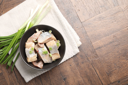 Pieces of delicious herring with green onions on wooden table, top view. Space for textの写真素材