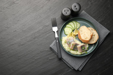 Pieces of delicious herring, mashed potato, cucumber slices and bread served on black table, flat lay. Space for textの写真素材
