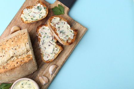 Tasty bread with garlic, herbs and butter on light blue background, top view. Space for textの写真素材