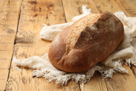 Fresh loaf of bread on wooden table, closeup. Space for text