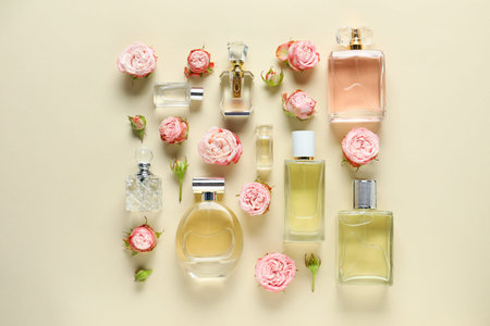 Bottles of perfume and beautiful flowers on beige background, flat lay