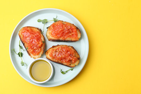 Tasty bread with tomato, microgreens and oil on yellow background, top view. Space for textの写真素材