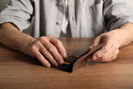Senior man with wallet counting coins at wooden table, closeup. Financial problemsの写真素材