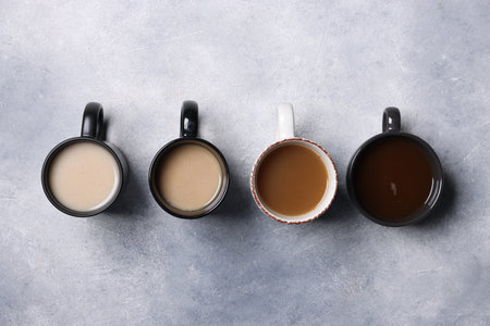Different cups with aromatic coffee drinks on grey textured table, flat layの写真素材