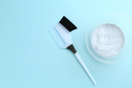 Bowl with hair bleaching powder and brush on light blue background, top view. Space for textの写真素材
