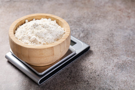 Digital kitchen scale with bowl of flour on grey textured table, closeupの写真素材