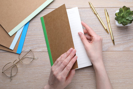 Woman with copybook and other stationery at wooden table, top view