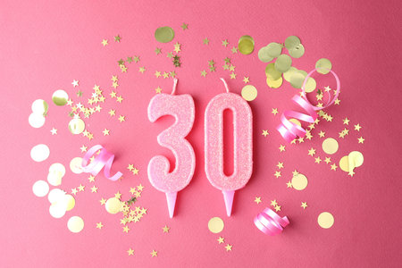 30th birthday. Number shaped candles and confetti on pink background, flat lay