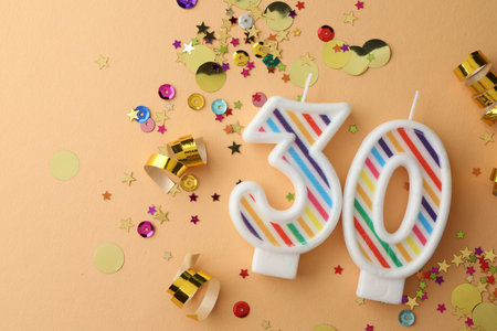 30th birthday. Number shaped candles and confetti on beige background, flat lay. Space for text