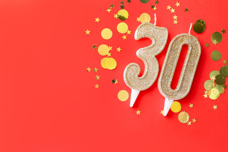 30th birthday. Number shaped candles and confetti on red background, flat lay. Space for textの写真素材